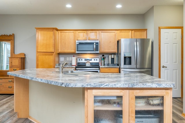 kitchen featuring sink, light brown cabinets, stainless steel appliances, light hardwood / wood-style floors, and a center island with sink