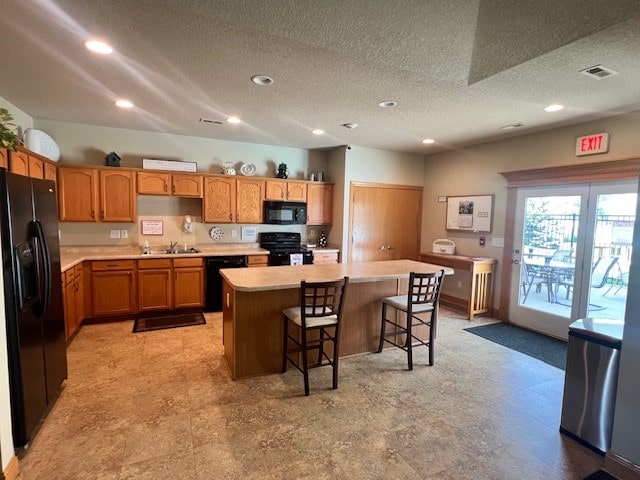 kitchen with black appliances, sink, a textured ceiling, a kitchen island, and a breakfast bar area