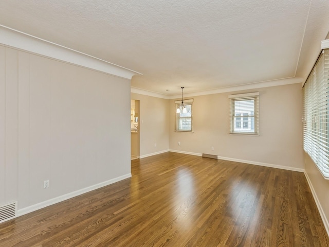 unfurnished room featuring a textured ceiling, dark wood-type flooring, crown molding, and a chandelier