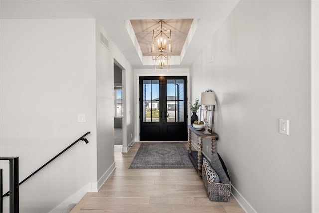 foyer entrance with a chandelier, a raised ceiling, french doors, and light hardwood / wood-style flooring