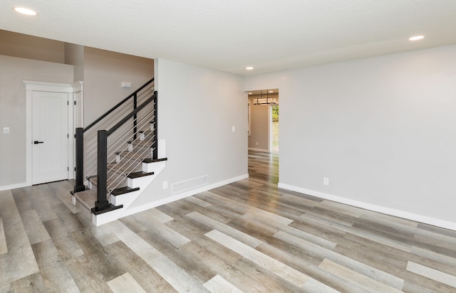 unfurnished room featuring a textured ceiling, light hardwood / wood-style floors, and an inviting chandelier