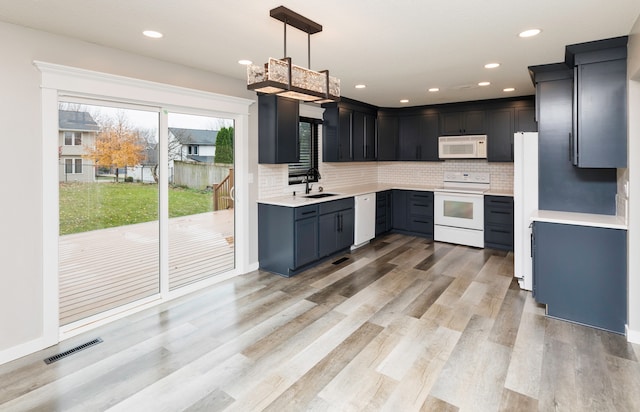 kitchen with pendant lighting, white appliances, sink, light wood-type flooring, and tasteful backsplash