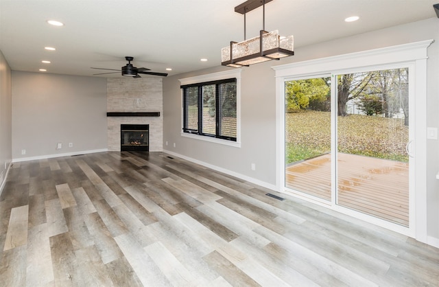 unfurnished living room with plenty of natural light, ceiling fan, wood-type flooring, and a tiled fireplace