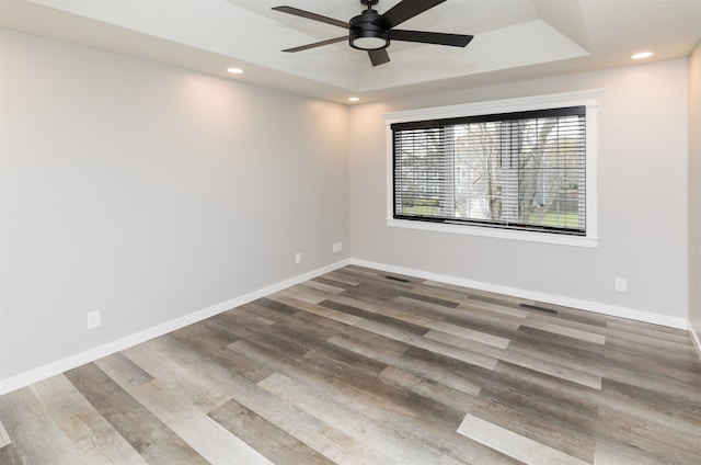 spare room with hardwood / wood-style flooring, ceiling fan, and a raised ceiling