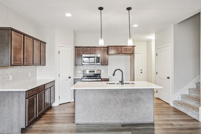 kitchen featuring pendant lighting, a kitchen island with sink, sink, light wood-type flooring, and appliances with stainless steel finishes