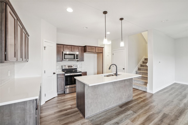 kitchen featuring decorative backsplash, appliances with stainless steel finishes, a kitchen island with sink, sink, and hardwood / wood-style floors