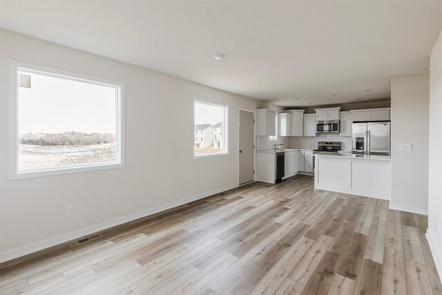 kitchen with white cabinetry, appliances with stainless steel finishes, decorative backsplash, and light hardwood / wood-style flooring