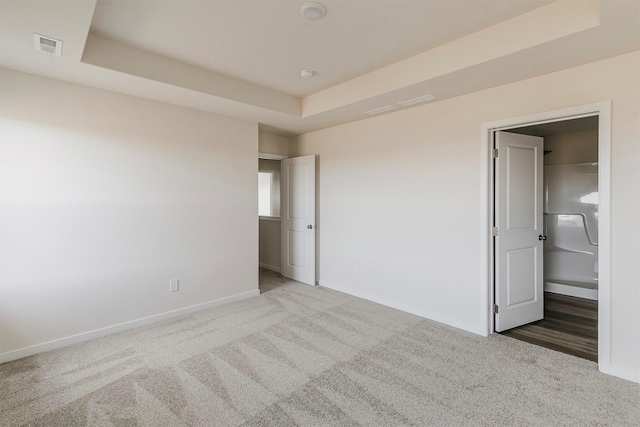 unfurnished bedroom with a tray ceiling and carpet floors