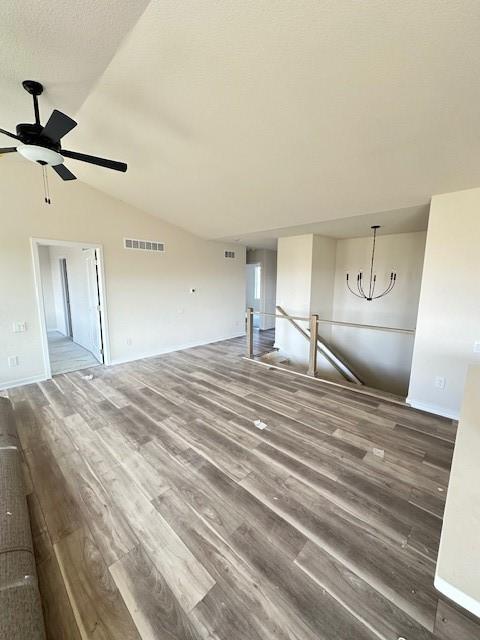 unfurnished living room featuring ceiling fan with notable chandelier, vaulted ceiling, and hardwood / wood-style flooring