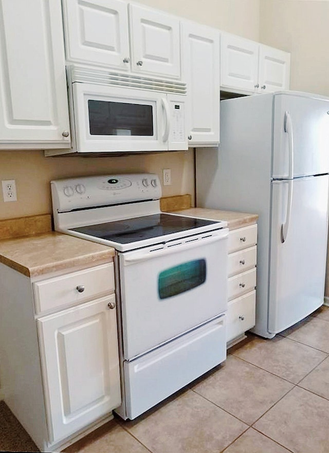 kitchen with light tile patterned floors, white cabinets, and white appliances