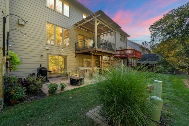 back house at dusk featuring a patio area, a lawn, and a balcony