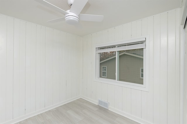 empty room with light hardwood / wood-style floors, ceiling fan, and wood walls