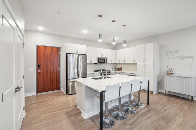 kitchen with white cabinets, appliances with stainless steel finishes, decorative light fixtures, and light hardwood / wood-style flooring