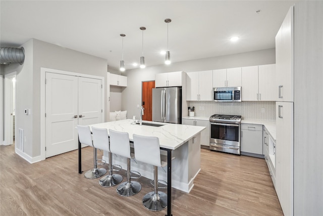 450 SW 7th St Unit 208, Des Moines, IA 50309 - kitchen featuring appliances with stainless steel finishes, a sink, light wood-type flooring, tasteful backsplash, and a kitchen island with sink