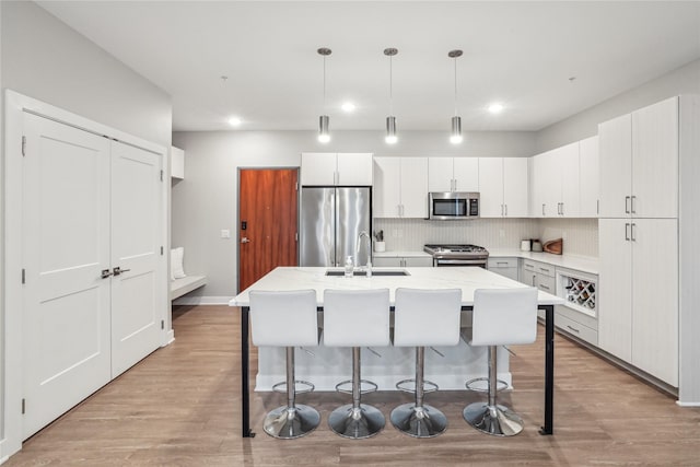 kitchen with stainless steel appliances, pendant lighting, white cabinets, and a center island with sink