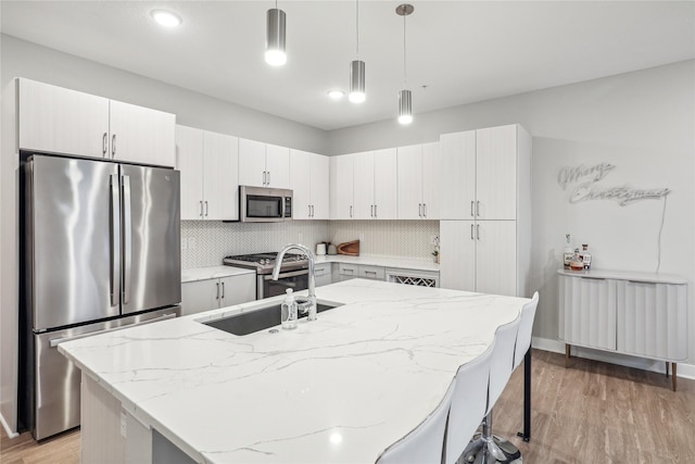 kitchen featuring stainless steel appliances, a sink, a kitchen breakfast bar, white cabinets, and pendant lighting