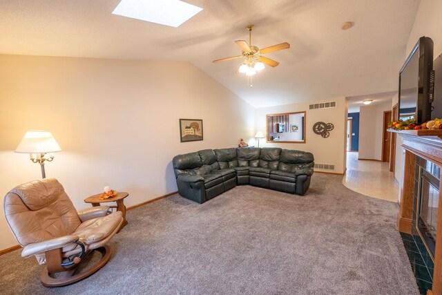 living room with a tile fireplace, carpet, ceiling fan, and vaulted ceiling with skylight