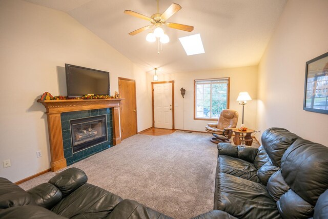 carpeted living room featuring a fireplace, ceiling fan, and vaulted ceiling with skylight