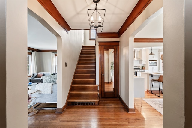 stairway with hardwood / wood-style flooring, ornamental molding, and a notable chandelier