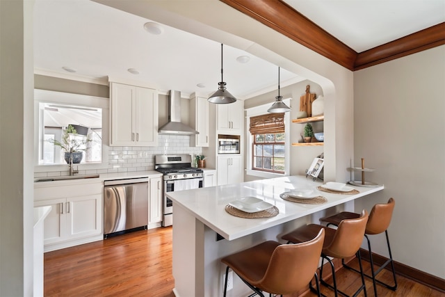 kitchen with wall chimney exhaust hood, white cabinetry, a breakfast bar, and appliances with stainless steel finishes