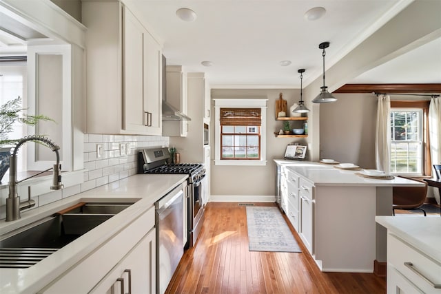 kitchen with appliances with stainless steel finishes, sink, pendant lighting, white cabinets, and light hardwood / wood-style floors