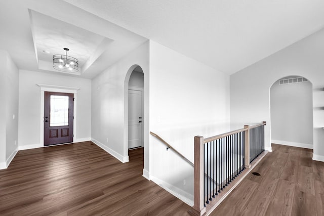 foyer with dark wood-type flooring, a tray ceiling, and a chandelier