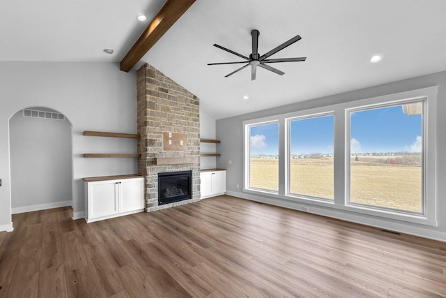 unfurnished living room featuring ceiling fan, a fireplace, lofted ceiling with beams, and hardwood / wood-style floors