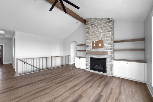 unfurnished living room featuring a stone fireplace, lofted ceiling with beams, light hardwood / wood-style floors, and ceiling fan