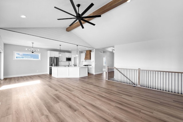 unfurnished living room with lofted ceiling with beams, sink, ceiling fan with notable chandelier, and light wood-type flooring