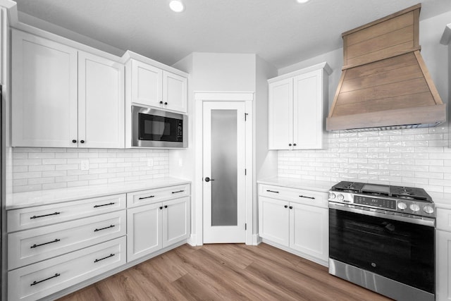 kitchen featuring built in microwave, gas range, custom exhaust hood, and white cabinets