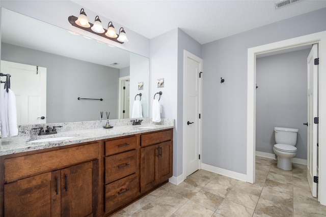 bathroom with a sink, baseboards, toilet, and double vanity