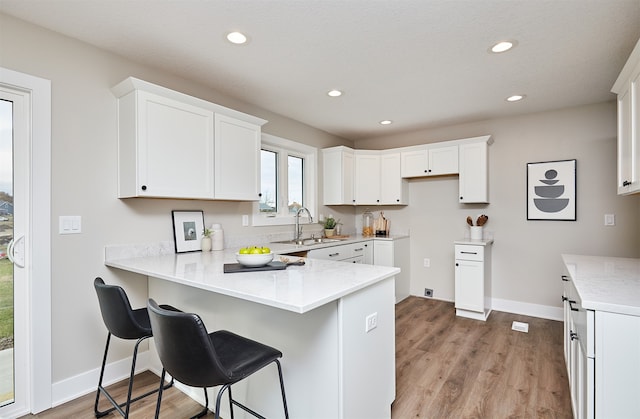 kitchen featuring white cabinets, light hardwood / wood-style floors, kitchen peninsula, and sink