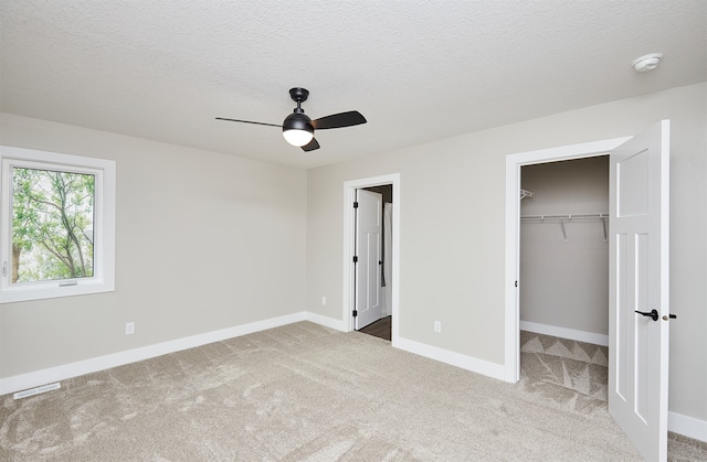 unfurnished bedroom featuring carpet, ceiling fan, a spacious closet, a textured ceiling, and a closet