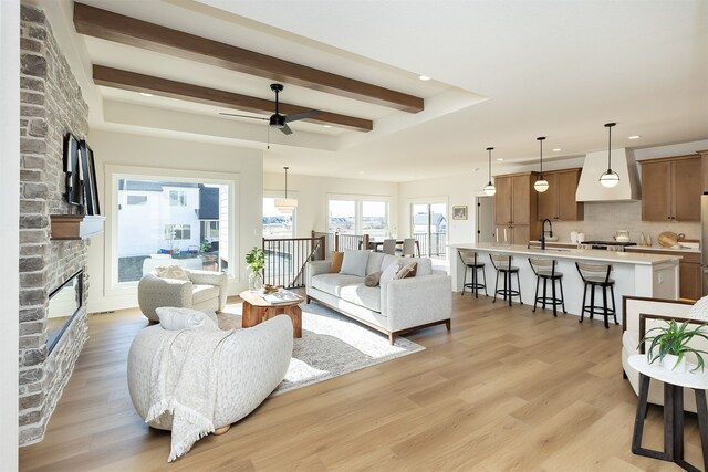 living room with light hardwood / wood-style flooring, ceiling fan, sink, beam ceiling, and a fireplace