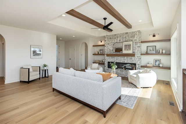 living room featuring built in shelves, light hardwood / wood-style flooring, a stone fireplace, and ceiling fan