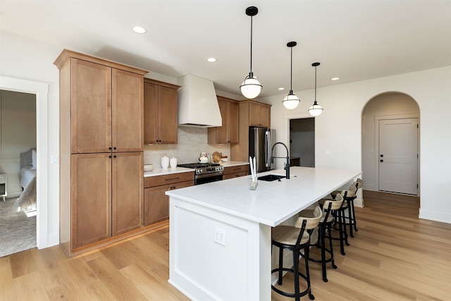 kitchen with pendant lighting, custom range hood, sink, a center island with sink, and stainless steel appliances