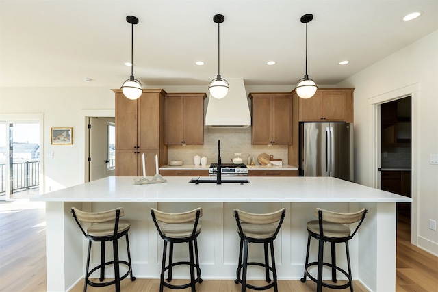 kitchen featuring brown cabinets, a spacious island, custom range hood, decorative backsplash, and freestanding refrigerator