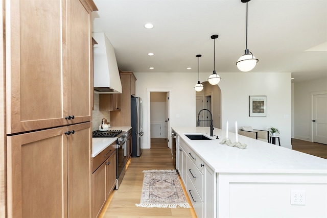 kitchen featuring custom exhaust hood, decorative light fixtures, white cabinetry, stainless steel appliances, and a kitchen island with sink