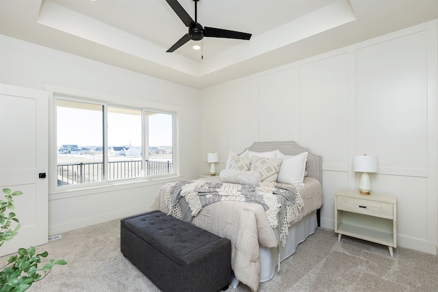 bedroom featuring ceiling fan, a water view, light colored carpet, and a tray ceiling