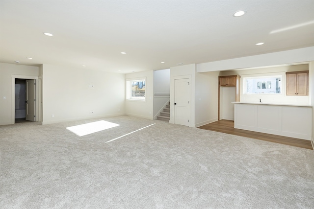 unfurnished living room featuring stairs, light carpet, baseboards, and recessed lighting