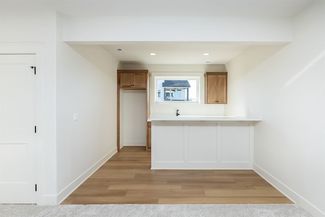 kitchen featuring baseboards, brown cabinets, a peninsula, light countertops, and light wood-type flooring