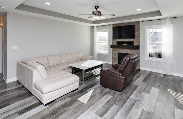 living room with a raised ceiling, ceiling fan, and dark hardwood / wood-style flooring