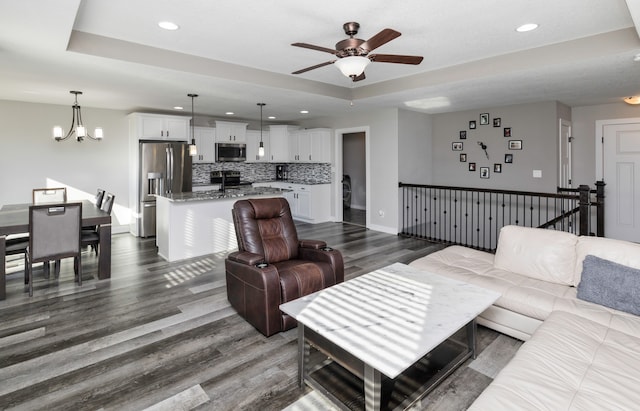 living room featuring ceiling fan with notable chandelier, dark hardwood / wood-style flooring, and a tray ceiling