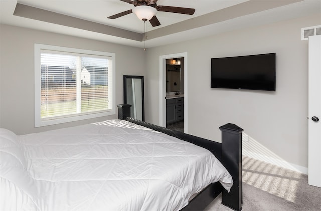 bedroom with carpet flooring, ceiling fan, a raised ceiling, and connected bathroom