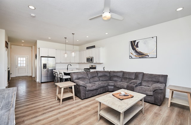 living room featuring ceiling fan, sink, a textured ceiling, and light wood-type flooring