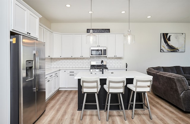 kitchen with a kitchen island with sink, white cabinets, light wood-type flooring, appliances with stainless steel finishes, and decorative light fixtures