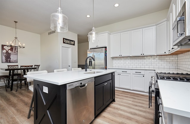 kitchen with stainless steel appliances, light hardwood / wood-style flooring, pendant lighting, a kitchen island with sink, and white cabinets