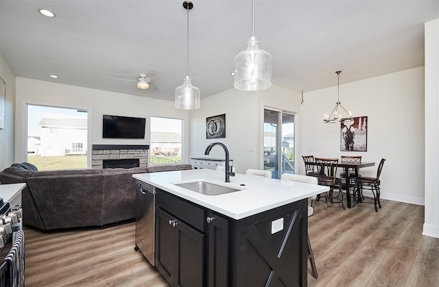 kitchen with sink, hanging light fixtures, stainless steel dishwasher, light wood-type flooring, and an island with sink