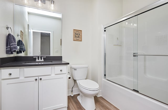 full bathroom with hardwood / wood-style floors, vanity, toilet, and bath / shower combo with glass door