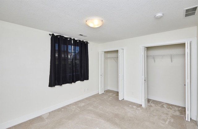 unfurnished bedroom featuring light carpet, a textured ceiling, and multiple closets